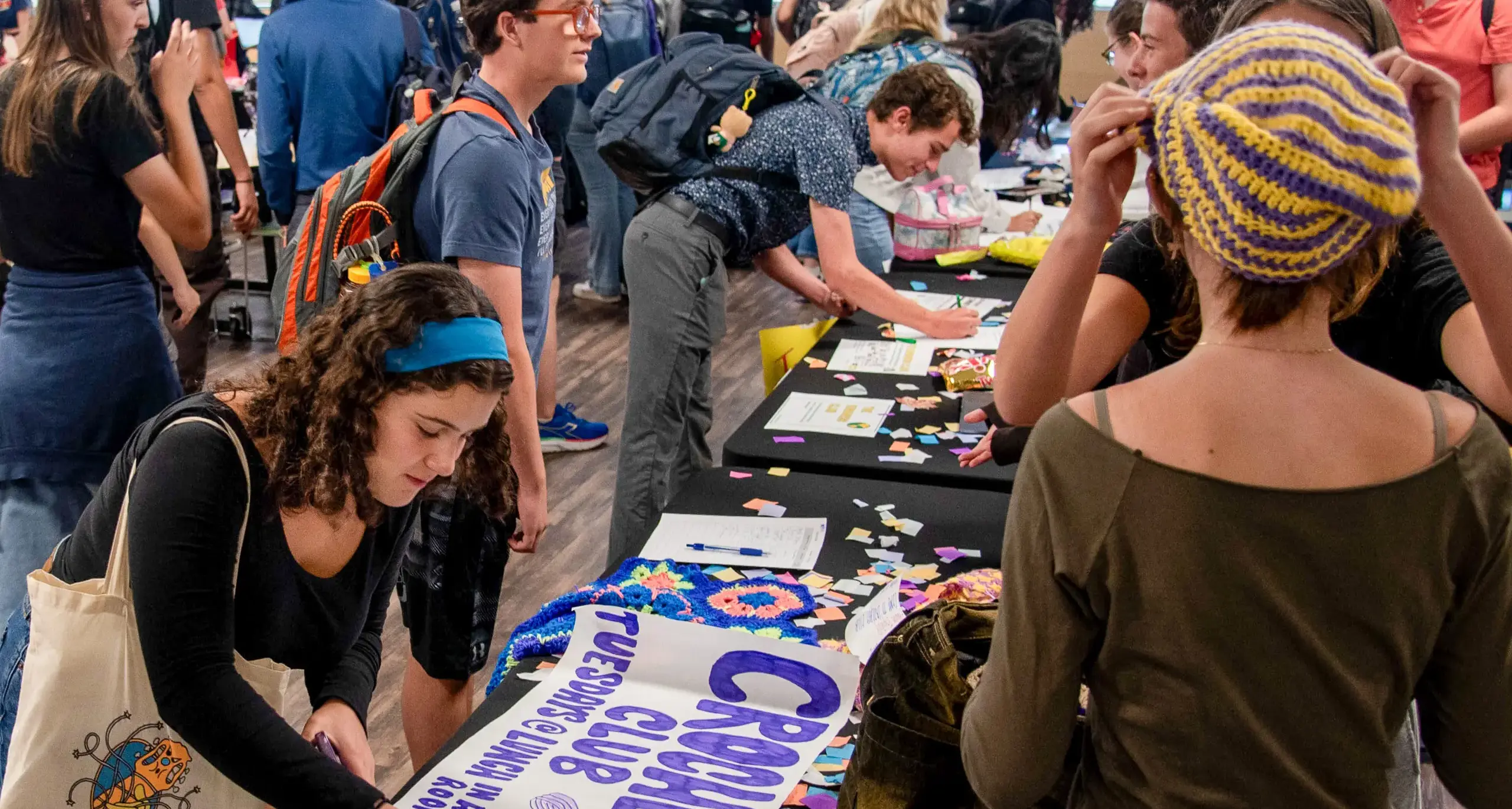 Several individuals gather around a table covered with signs, actively  participating in a conversation.