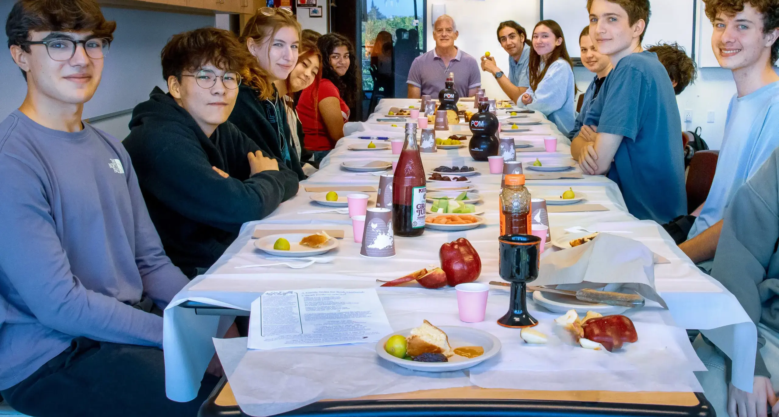 A long table filled with food, surrounded by a group of people engaged  in conversation and sharing a meal.