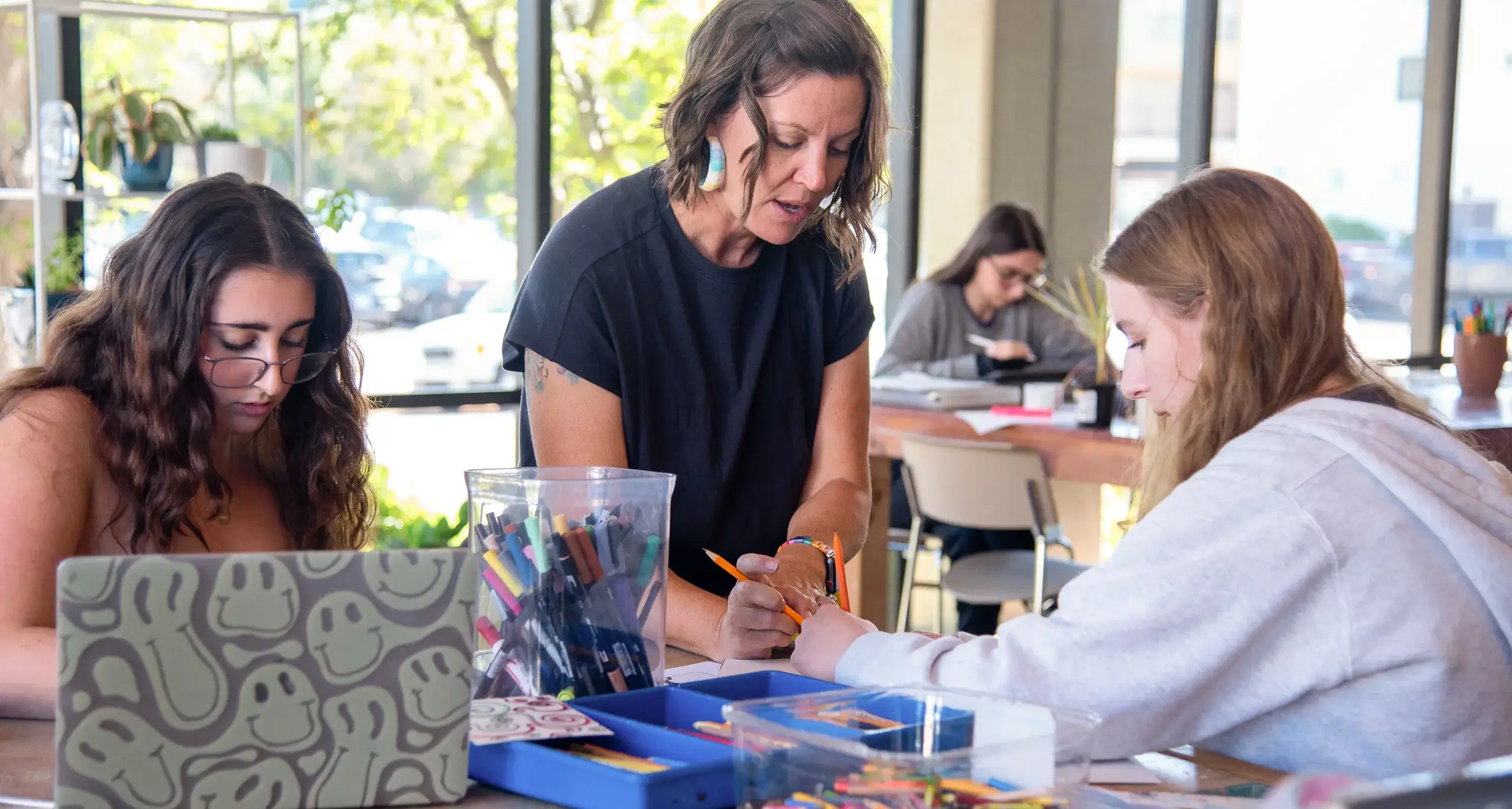 Two students and a teacher collaborating on a project at a table, surrounded by papers and laptops, focused on their work.