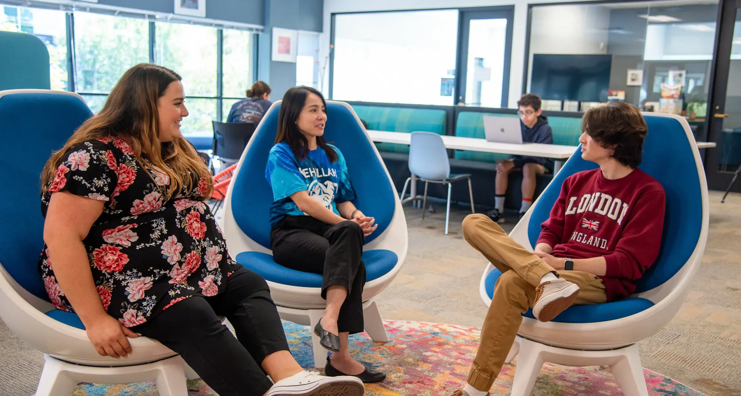 Two women college counselors converse with a male student while  seated in chairs, focusing on college guidance.