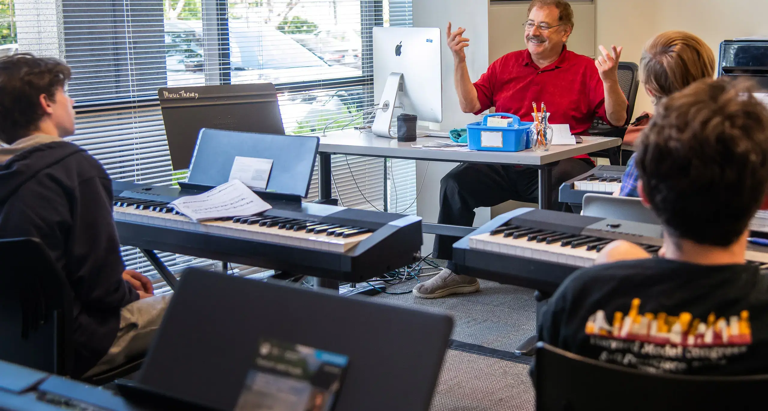 A group of students in a classroom with a teacher, each with a  keyboard.